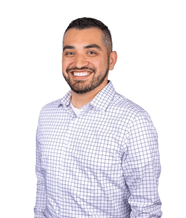 A man with short dark hair and a beard is smiling, wearing a white shirt with a blue plaid pattern, standing against a plain white background.