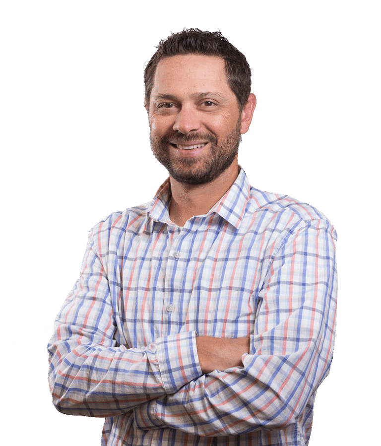 A man with short dark hair and a beard smiles with arms crossed, wearing a light-colored, plaid button-up shirt, standing against a plain white background.