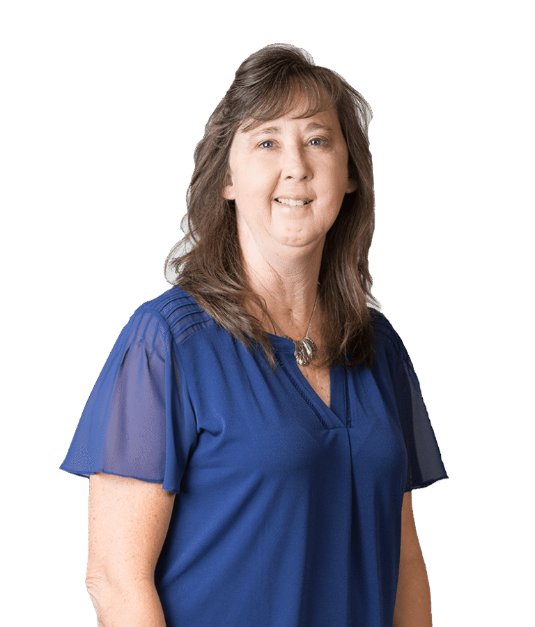 A woman with long brown hair wearing a royal blue short-sleeve blouse stands smiling against a plain, light background.