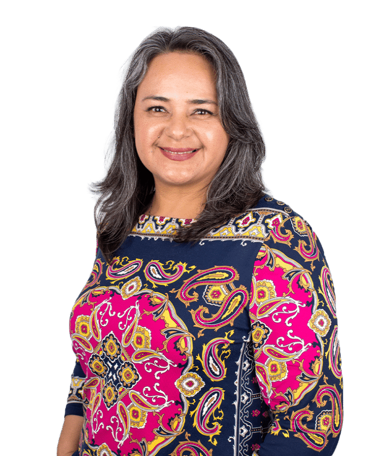 A smiling woman with long gray hair wearing a colorful, patterned top stands against a plain white background.