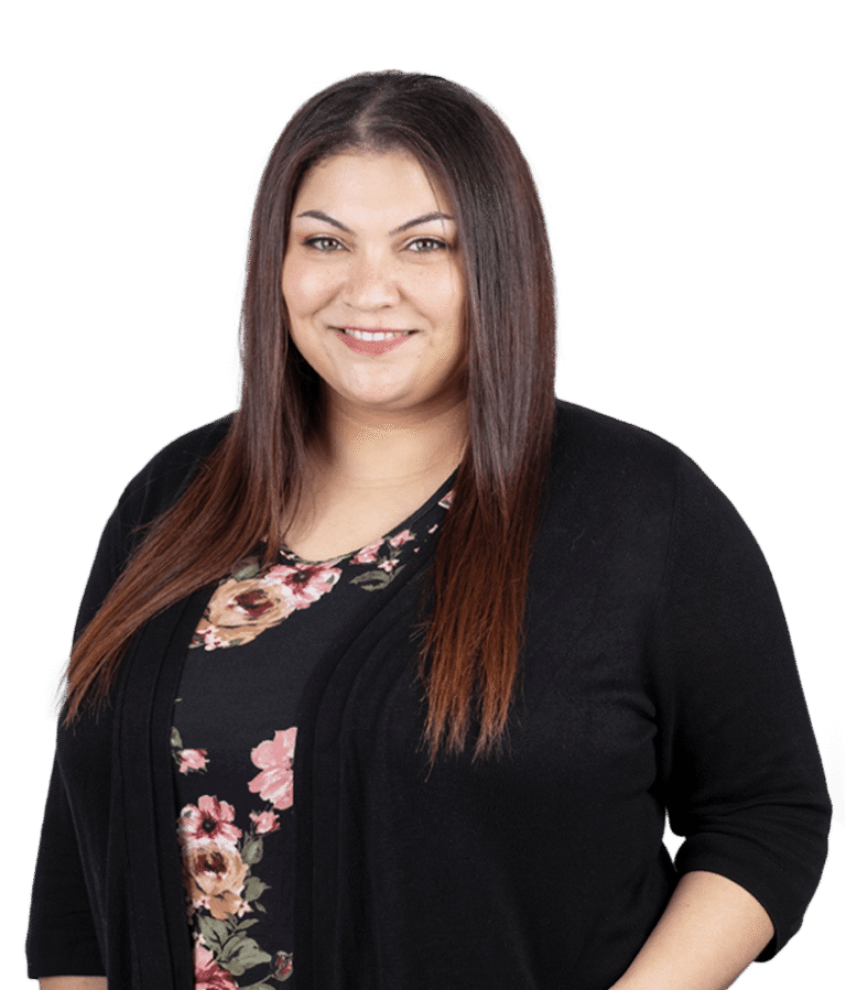 A woman with straight, long brown hair smiles at the camera. She is wearing a black cardigan over a floral-patterned top and is posed in front of a plain light background.