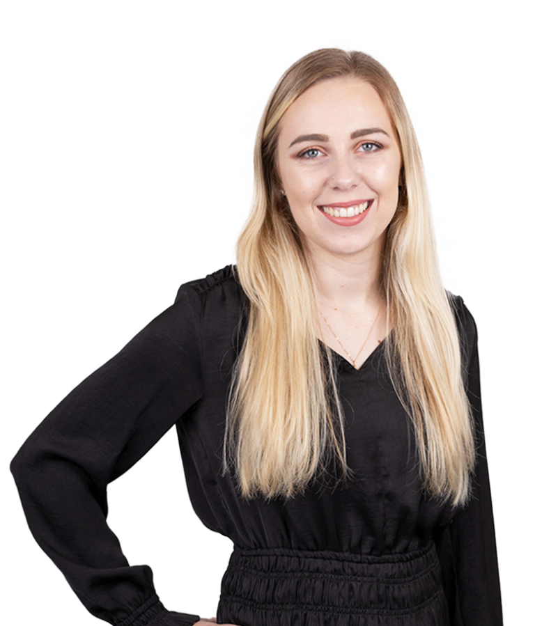 A woman with long blonde hair, wearing a black long-sleeve top, stands smiling with one hand on her hip against a plain white background.