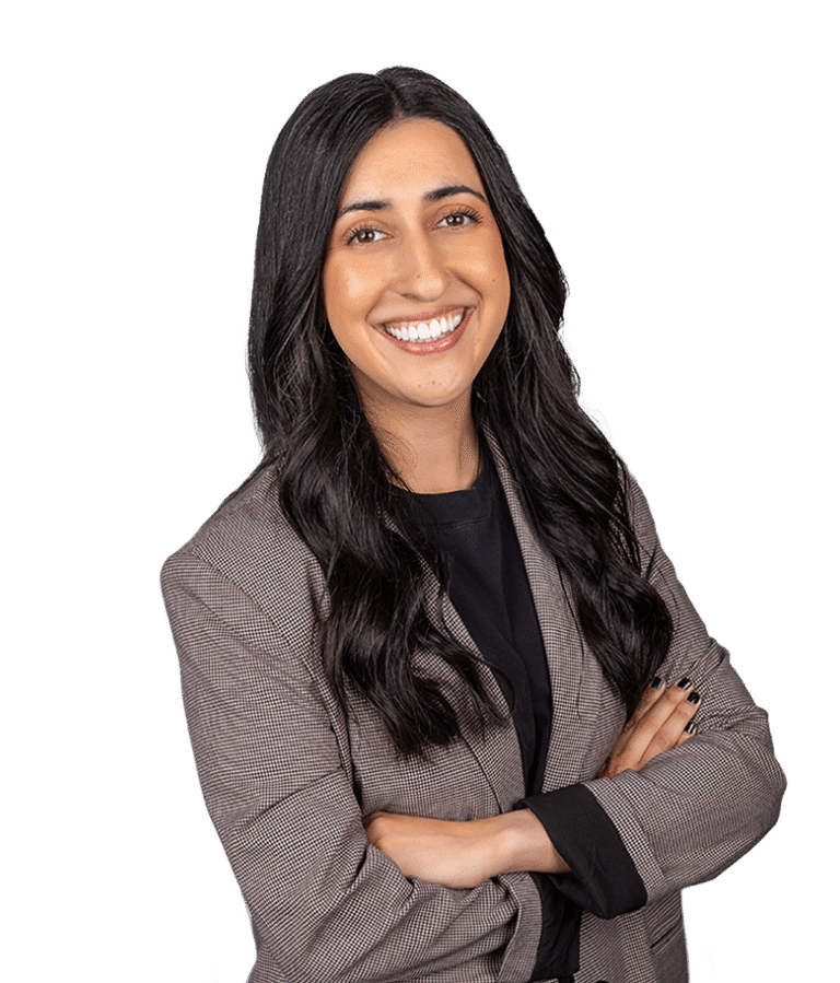 A woman with long dark hair, wearing a gray plaid blazer and black shirt, smiles confidently with her arms crossed against a plain white background.