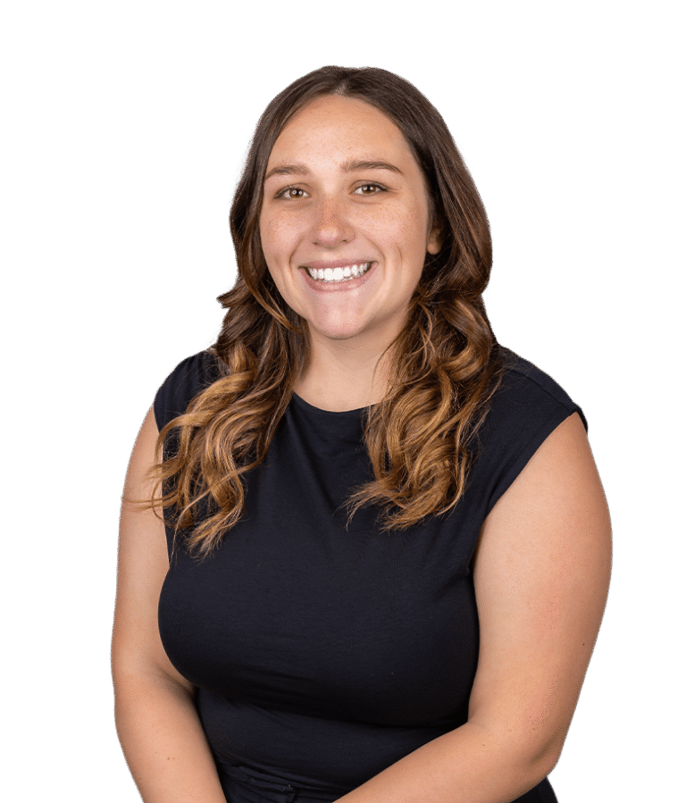 Smiling woman with long, wavy brown hair wearing a short-sleeve black top, posing against a plain white background.