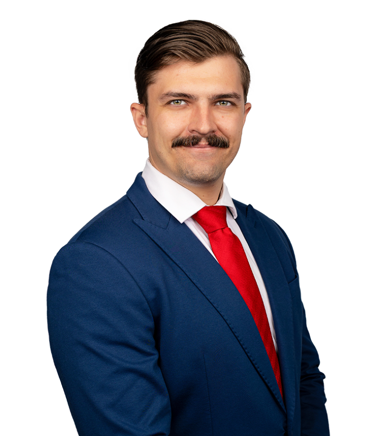 A man with short brown hair and a mustache, wearing a blue suit, white shirt, and red tie, poses confidently against a plain white background.