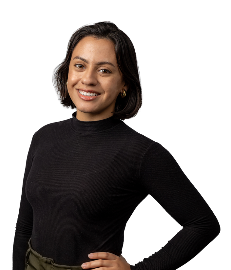 A woman with short dark hair, wearing a black long-sleeve top, stands smiling with one hand on her hip against a plain white background.