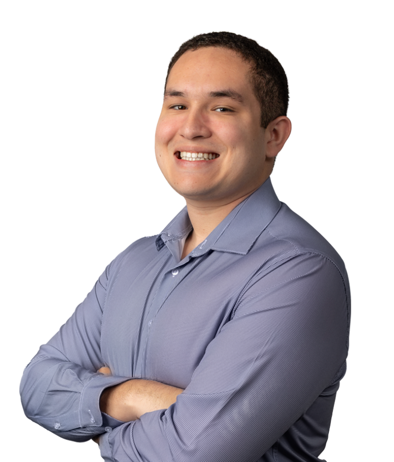 A young man with short, curly dark hair, wearing a light purple button-up shirt, stands smiling with his arms crossed against a plain white background.