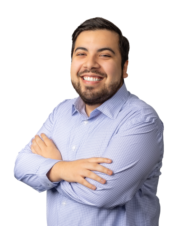 A smiling man with a beard and mustache stands with his arms crossed, wearing a light blue checkered shirt against a plain white background.