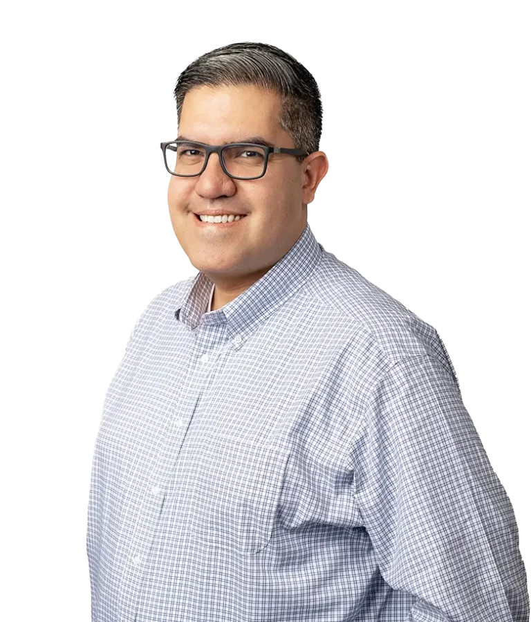 A man with short dark hair and glasses, wearing a light blue checkered button-up shirt, smiling and standing against a plain white background.