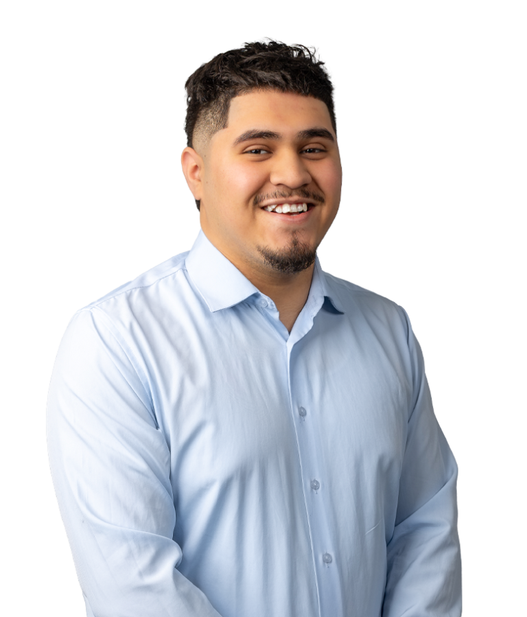 A smiling man with short dark hair and a goatee wearing a light blue button-up shirt stands against a plain white background.